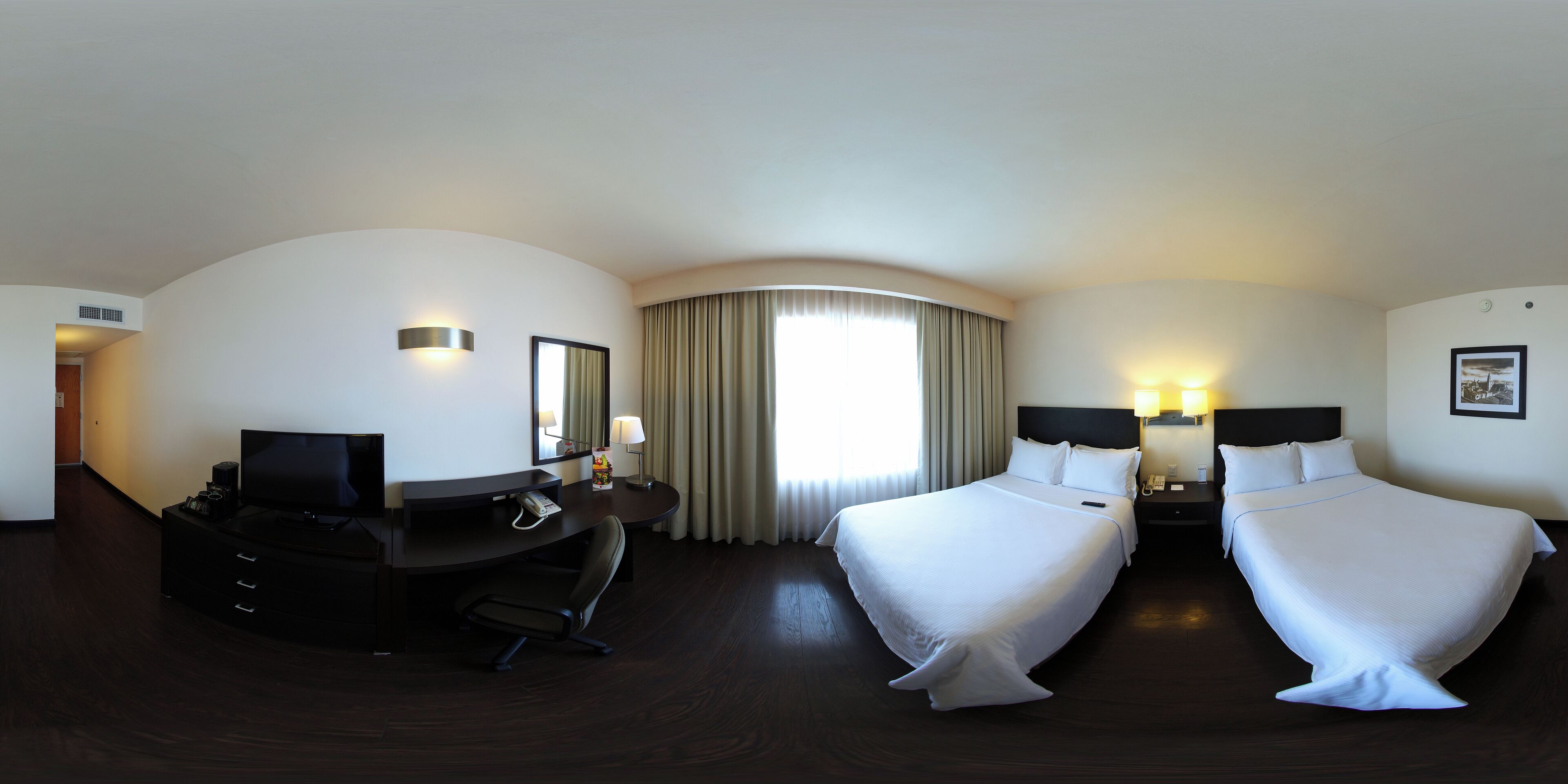 A hotel room with a large bed, a desk with a chair, a television, and a window with curtains.