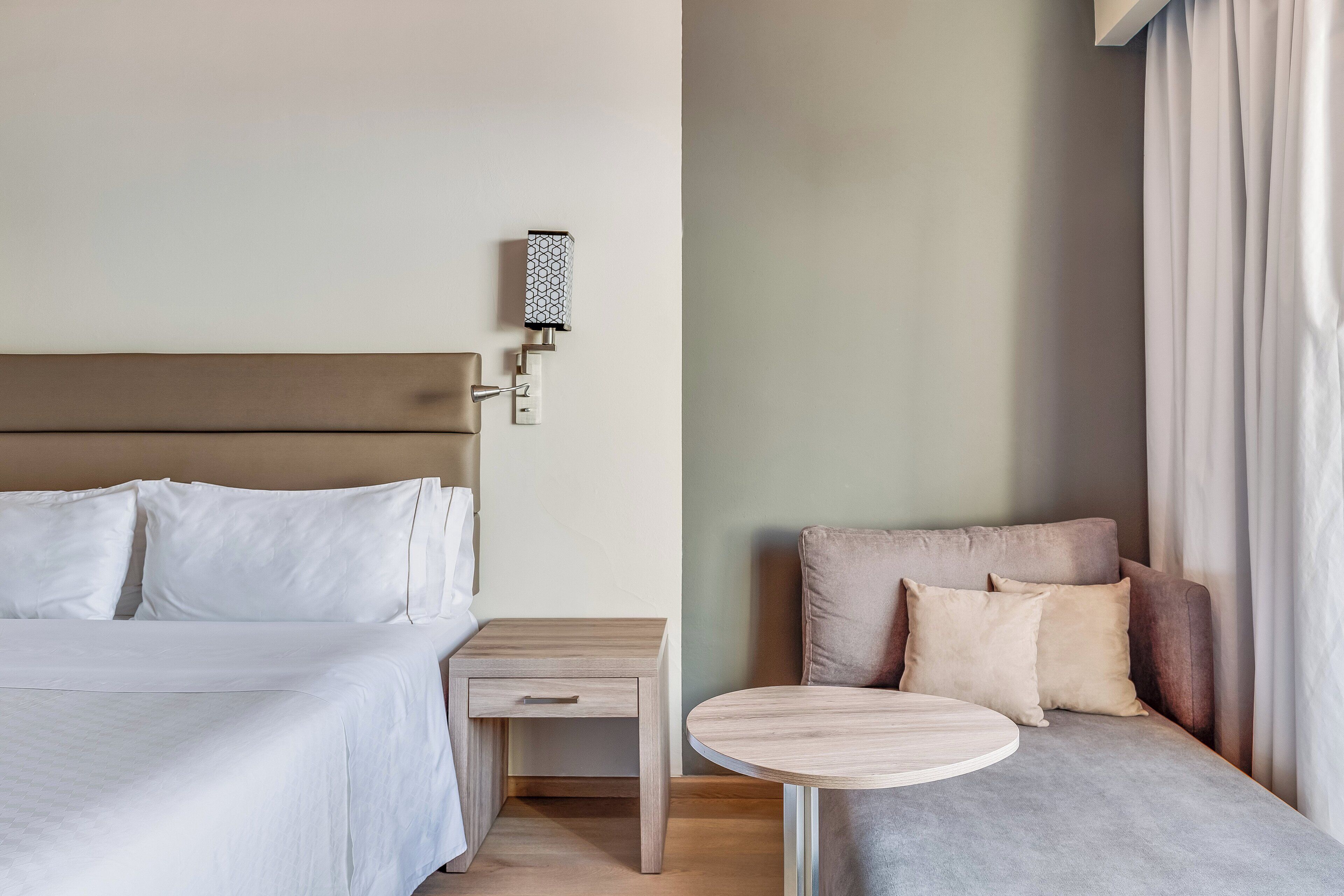 A hotel room with a bed, bedside table, and a small round table.