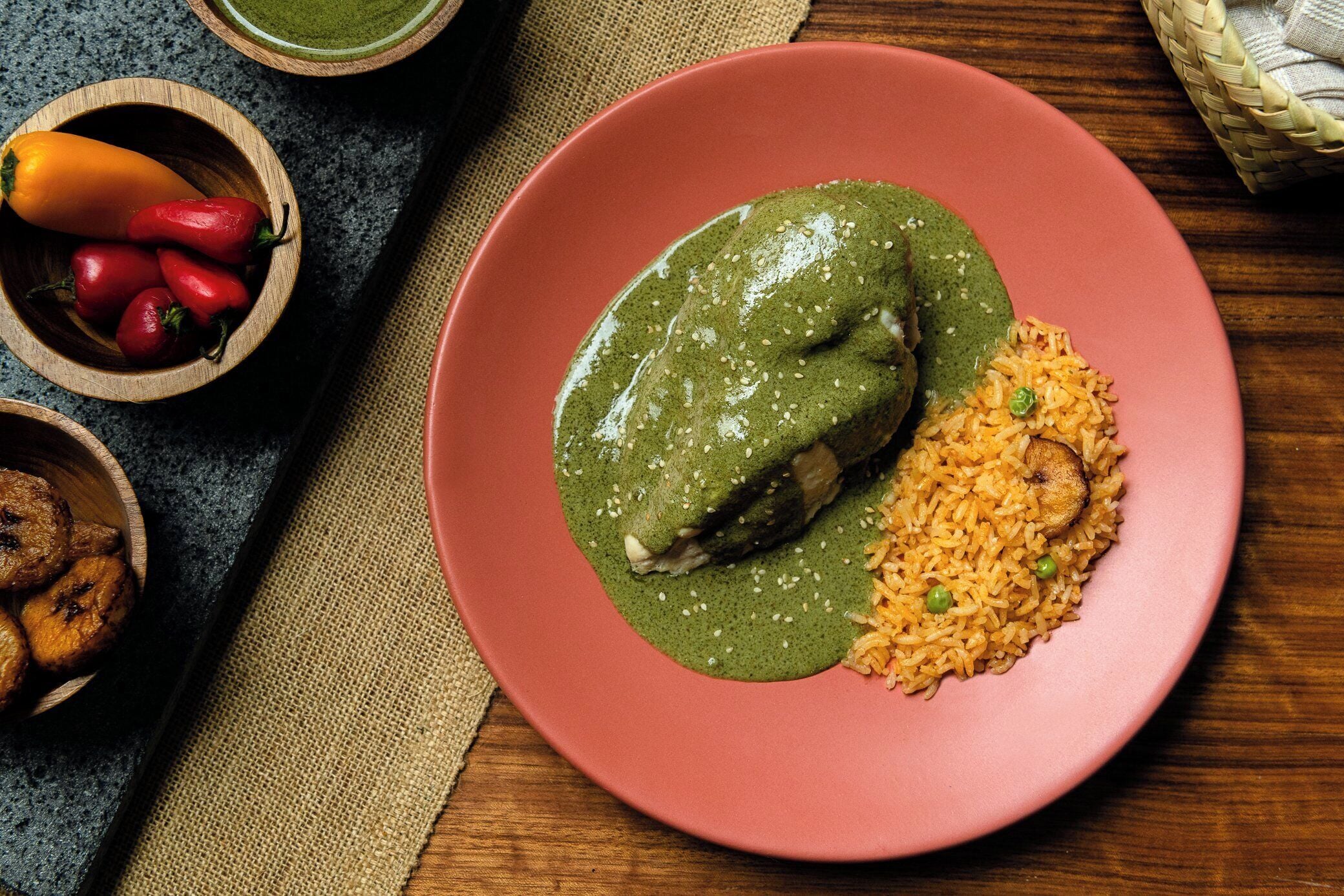 A plate with a green sauce-covered meat and rice, accompanied by bowls of vegetables and fruits.