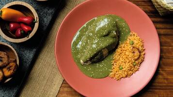 A plate with a green sauce-covered meat and rice, accompanied by bowls of vegetables and fruits.