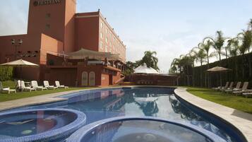 Zona de piscina amb gandules i ombrel·les, edifici Fiesta Inn i palmeres.
