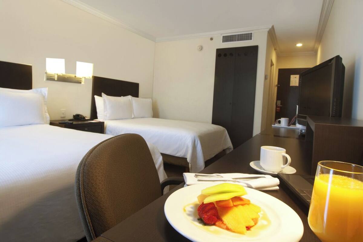 Habitación de hotel con dos camas, una mesa de comedor con desayuno, una taza de café y un vaso de jugo de naranja.