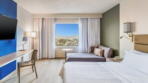 A hotel room with a bed, a desk, a chair, a small table, and a TV.