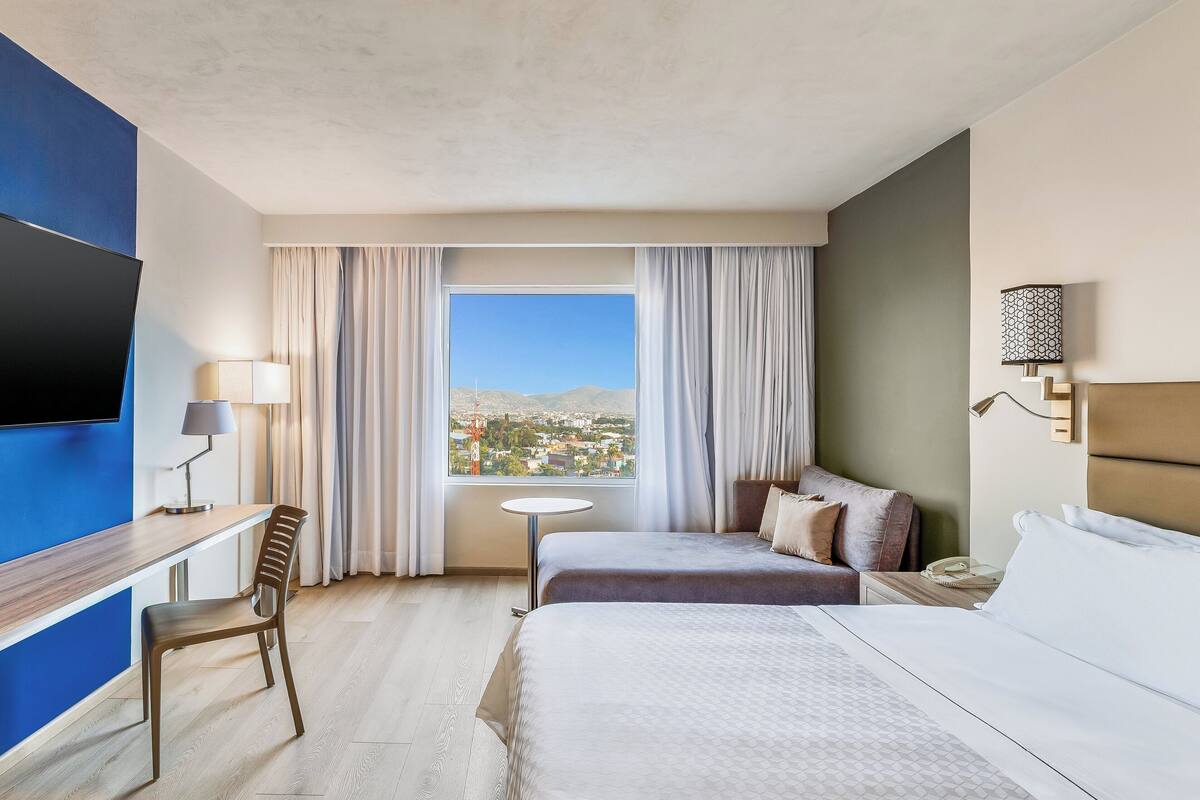 Una habitación de hotel con cama, escritorio, silla, mesita y televisión.