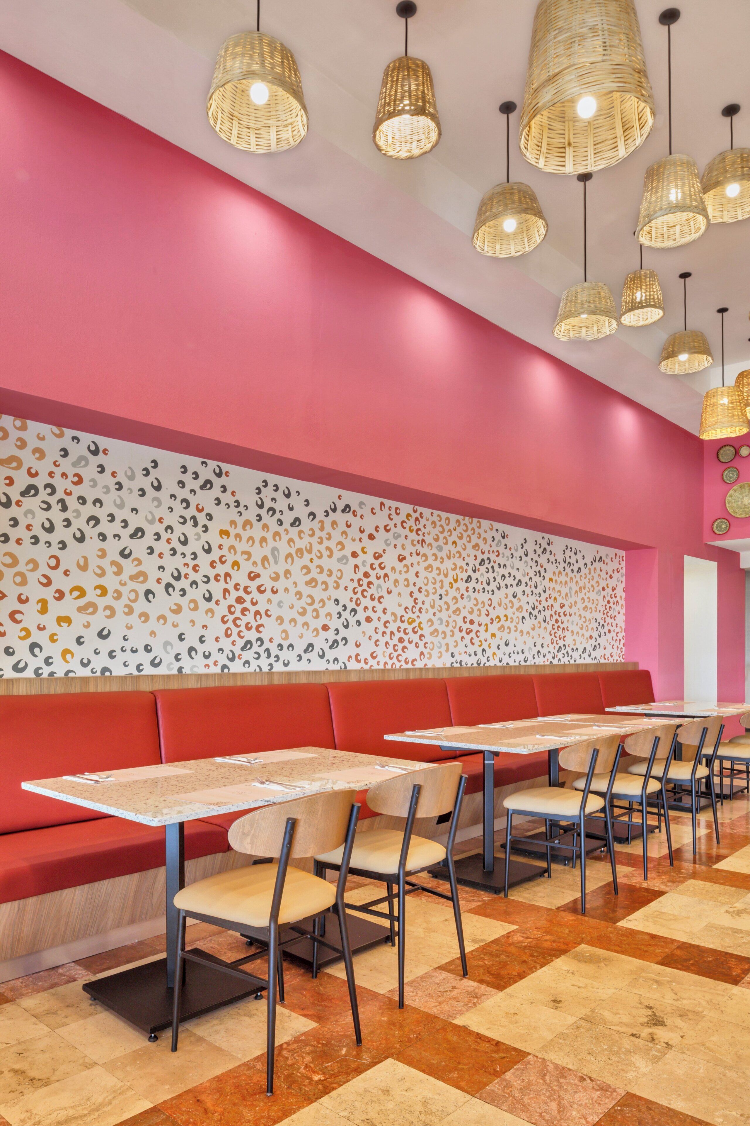 Un restaurante moderno con asientos rojos, varias mesas y lámparas colgantes tejidas.