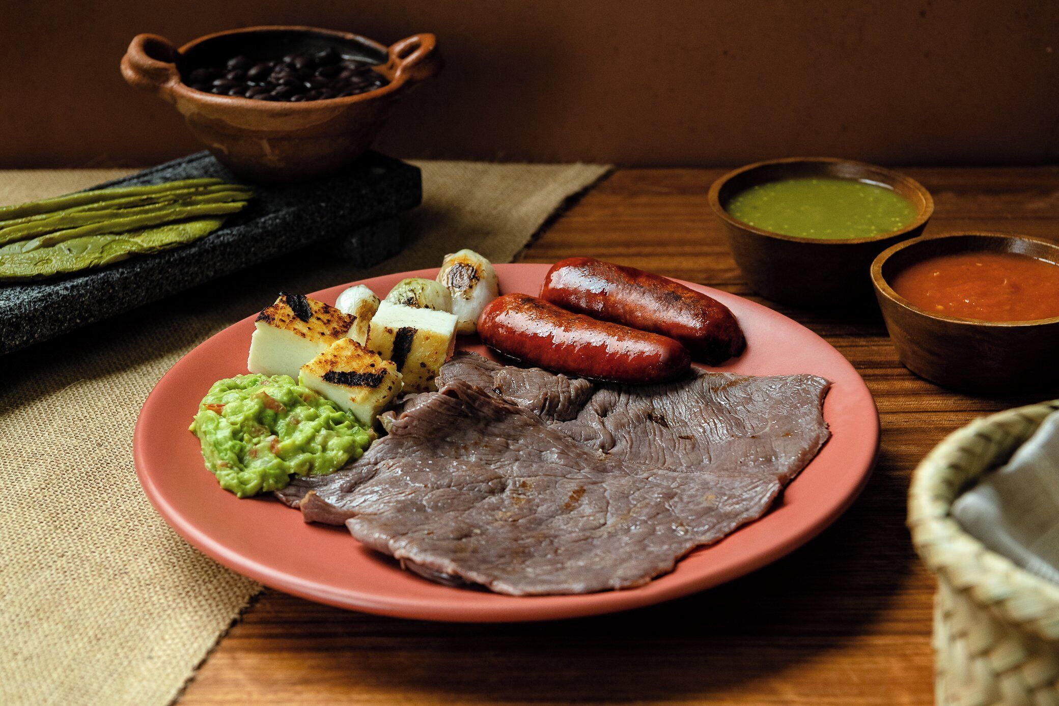 A plate with grilled meat, sausages, guacamole, and roasted potatoes.
