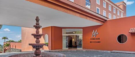 A courtyard with a fountain, a building with a sign reading 'tita COMEDOR MEXICANO', and a stone-paved ground.