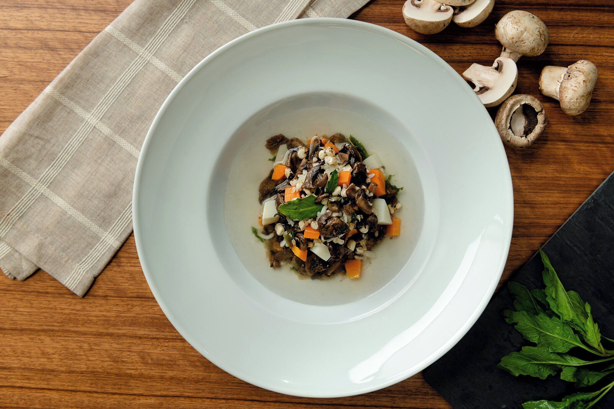 A white bowl of vegetable stir-fry on a wooden table with a checkered cloth.