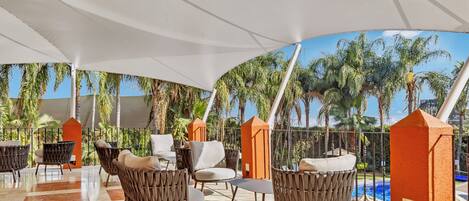 A covered outdoor seating area with wicker chairs and a pool in the background.