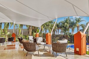 Un área de estar techada al aire libre con sillas de mimbre y una piscina al fondo.
