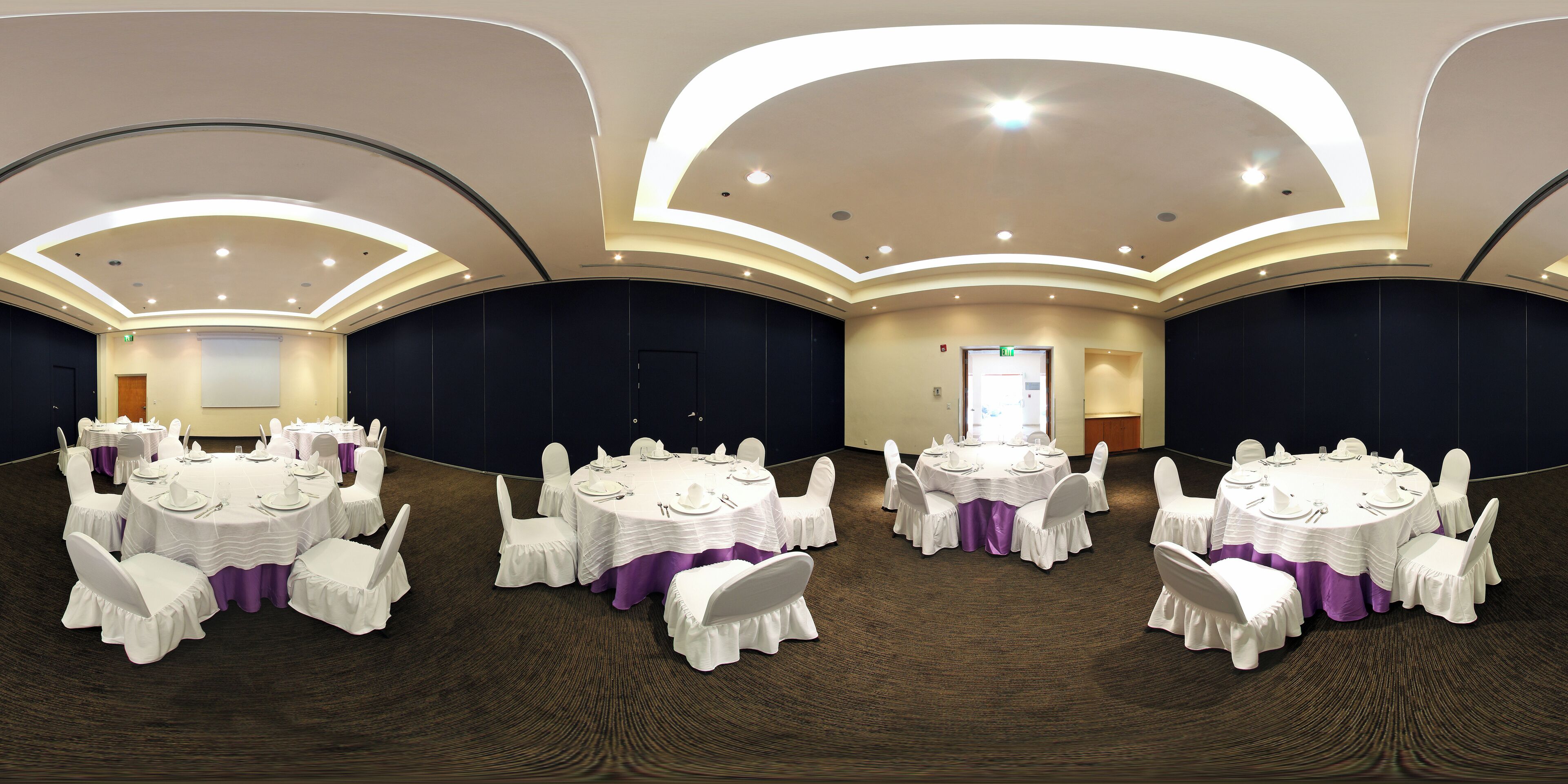 Un salón de conferencias con varias mesas redondas, sillas blancas y manteles morados.