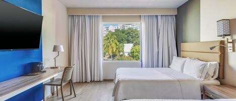 Habitación de hotel con cama, escritorio, silla, televisor y ventana con cortinas.