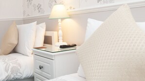 Una cama individual con ropa de cama estampada, una mesita de noche con lámpara y un mueble auxiliar con control remoto.