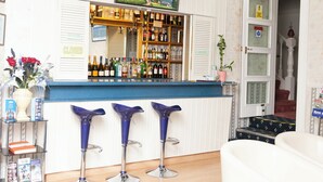 Zona de bar con mostrador, estantes llenos de botellas y tres taburetes azules.