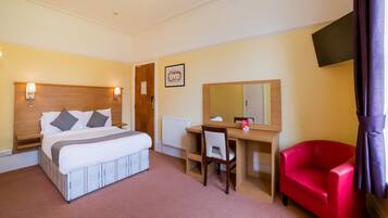 Een hotelkamer met een bed, bureau, stoel en een rode fauteuil.