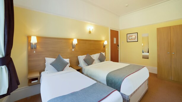 Quarto de hotel com duas camas, cabeceiras de madeira, luminárias de apoio, um guarda-roupa e um espelho.