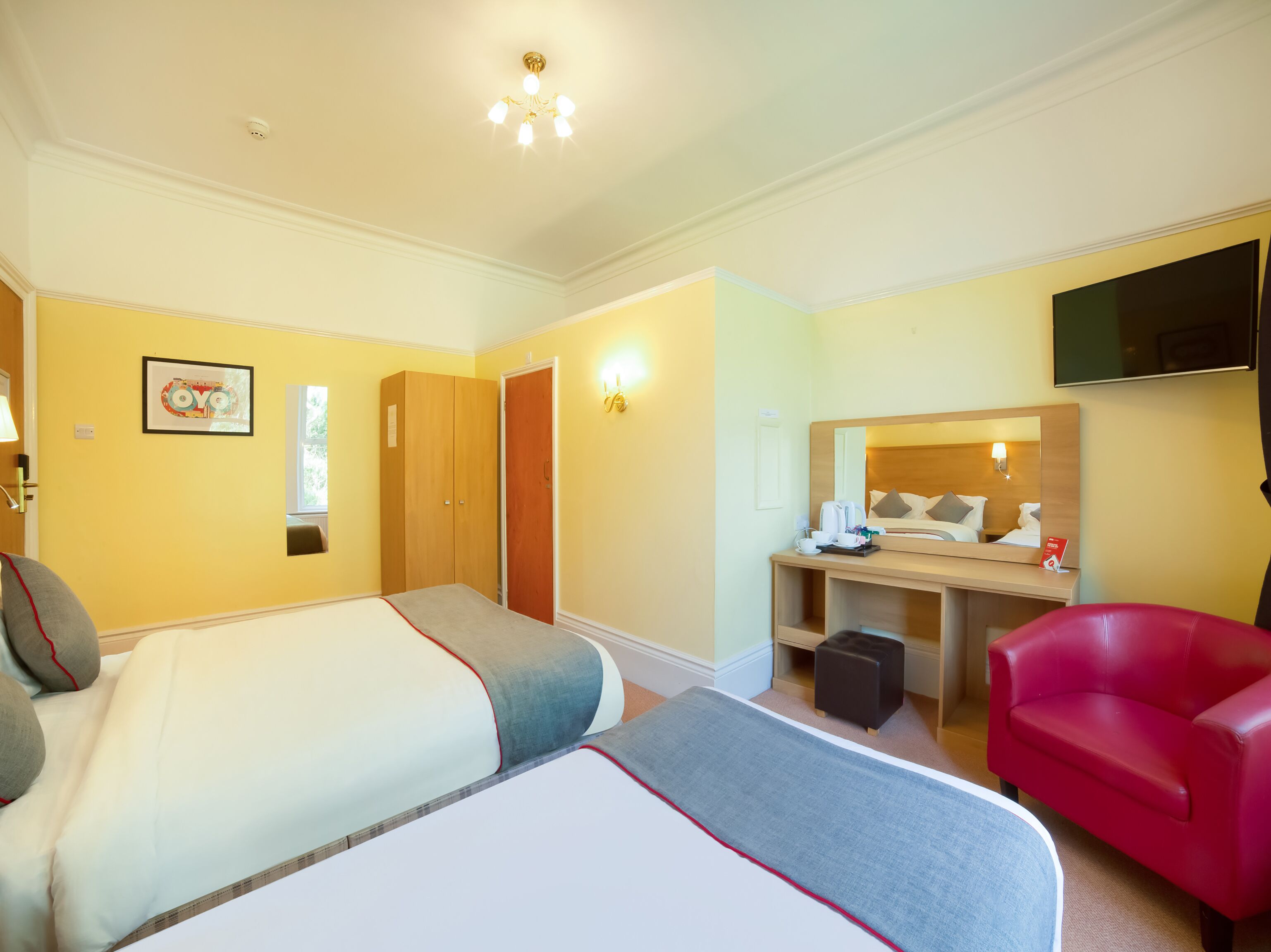 Habitación de hotel con dos camas, un escritorio con silla, televisor y un sillón rojo.