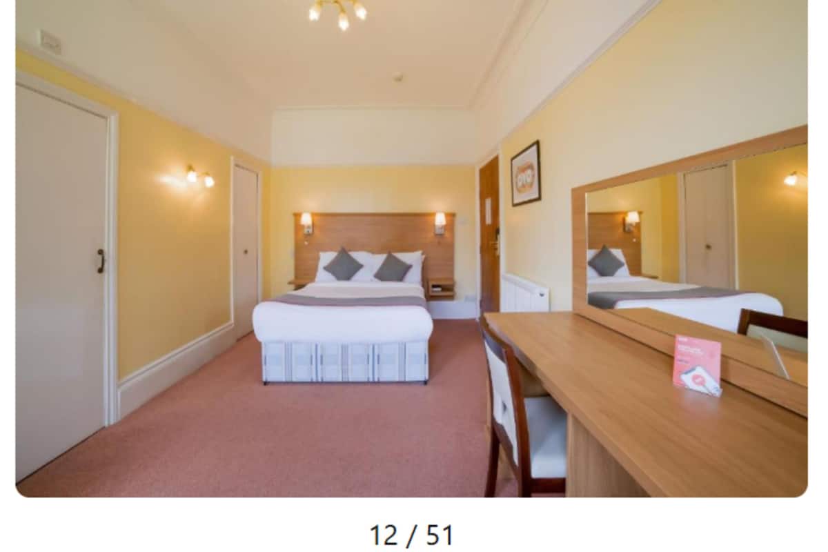 A hotel room with a bed, bedside tables, a desk, and a mirror.