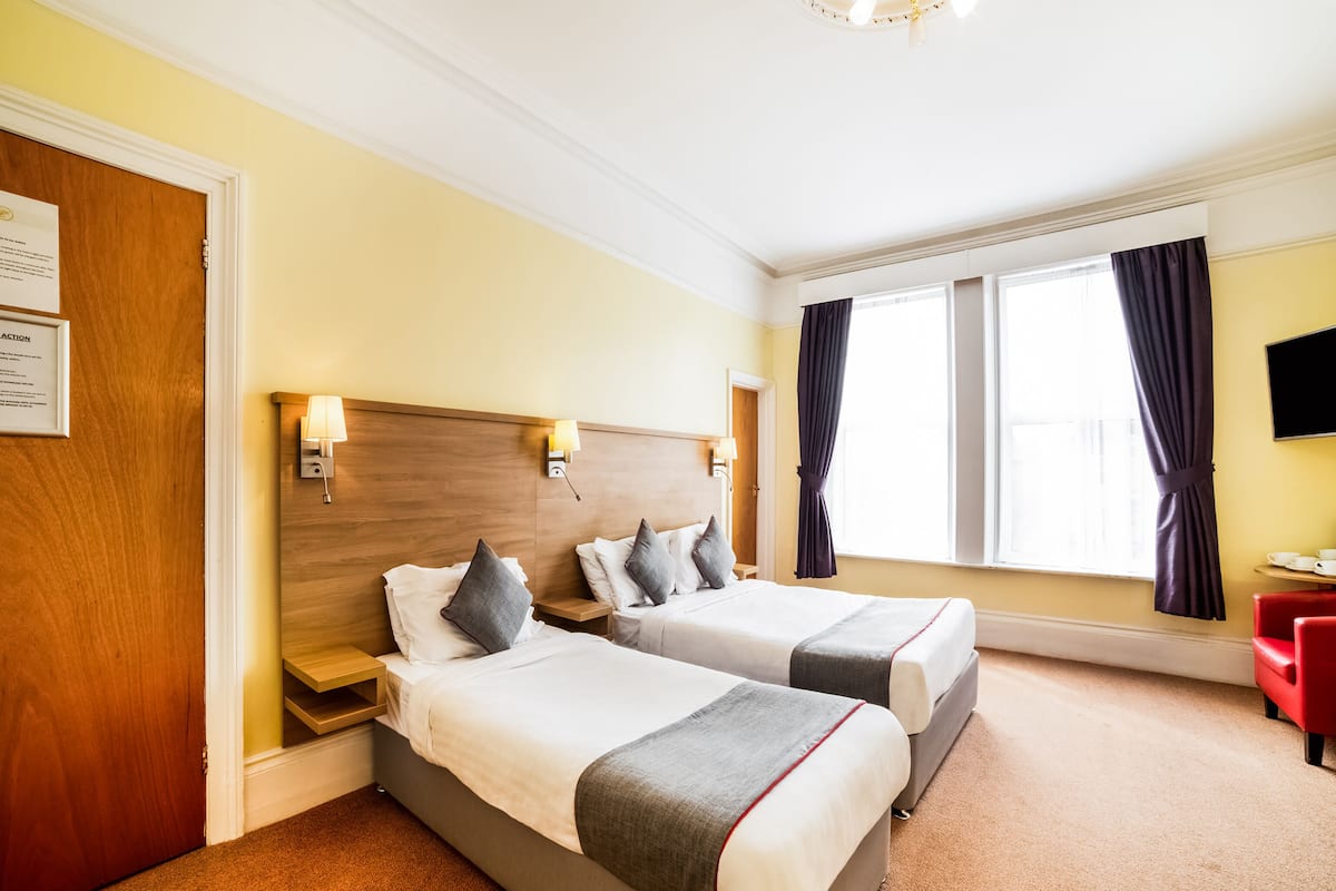 A hotel room with two beds, a wooden headboard, a flat-screen TV, and a window with curtains.