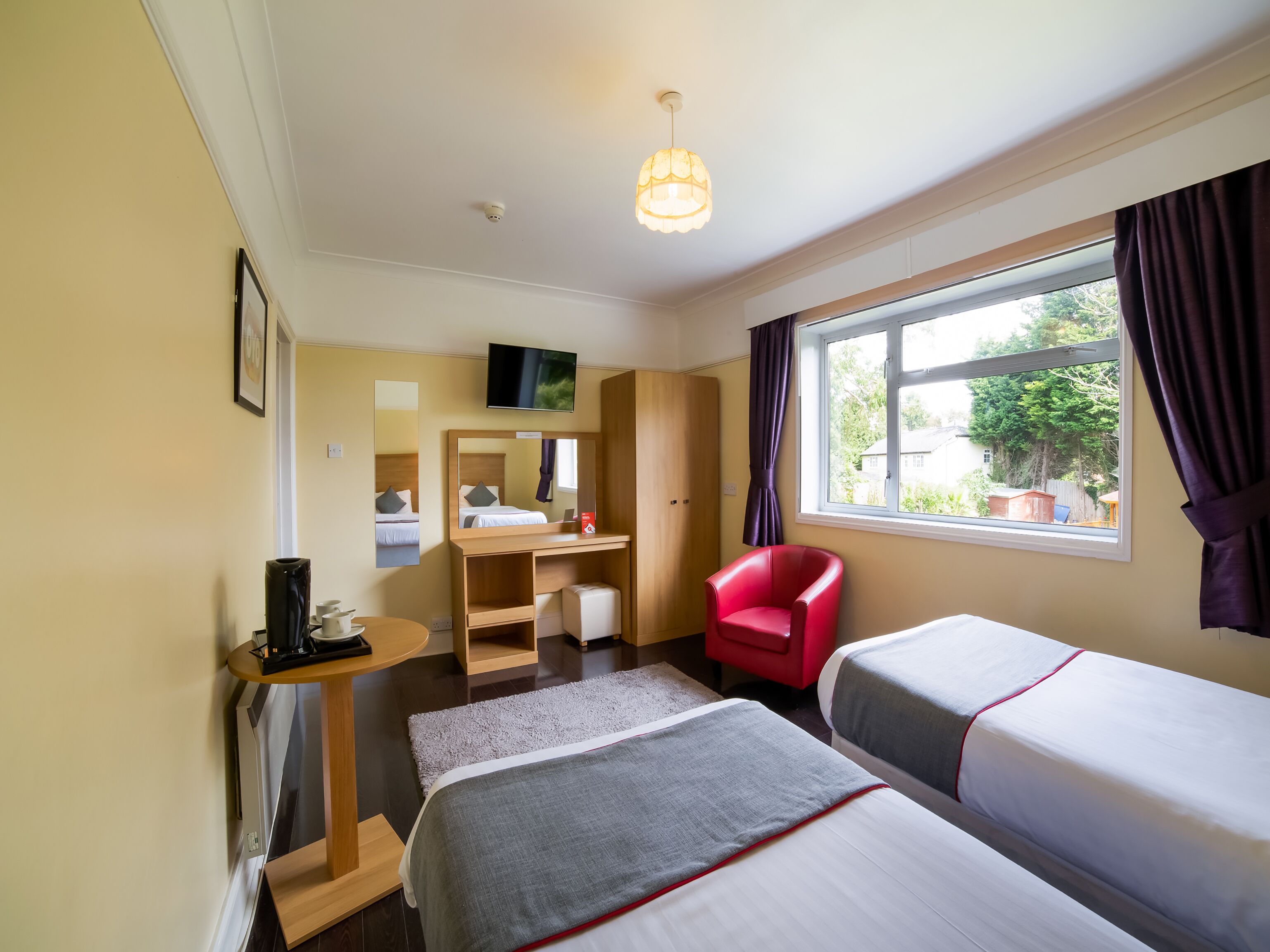 A hotel room with a bed, a desk, a chair, a TV, and a window with curtains.