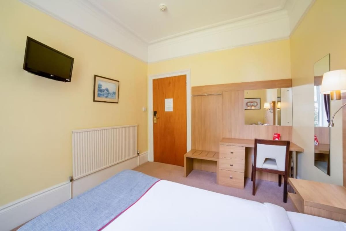 A hotel room with a bed, a desk, a chair, a television, a radiator, and a door.