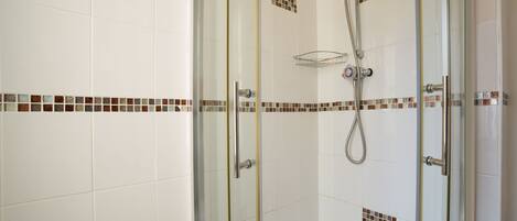 A glass-enclosed shower area with a handheld showerhead and a handheld showerhead with a hose.