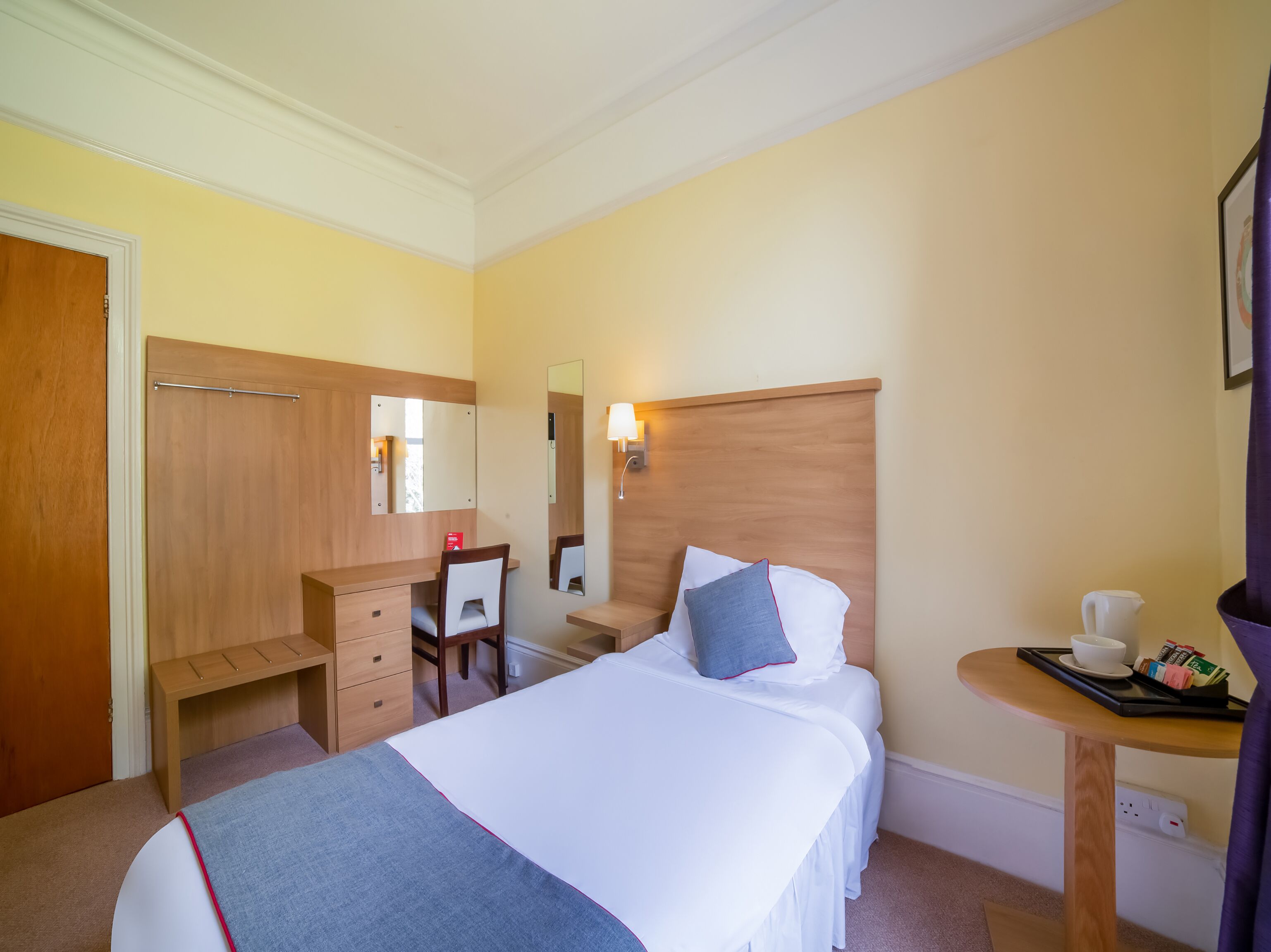 Une chambre d’hôtel comprenant un lit, un bureau, une chaise, une petite table avec un plateau contenant des articles pour le petit-déjeuner et un miroir.