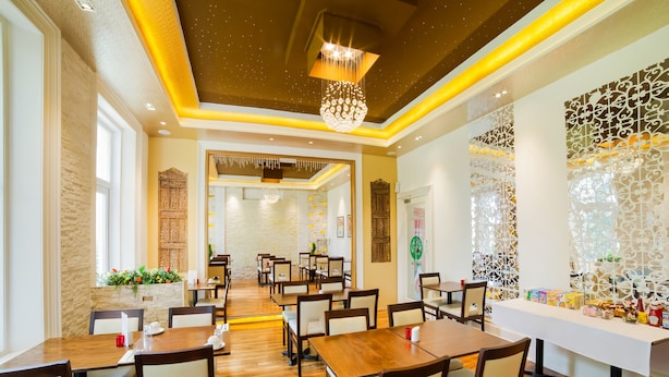 Un espaiós restaurant amb taules i cadires de fusta, panells decoratius a les parets i un penjador.