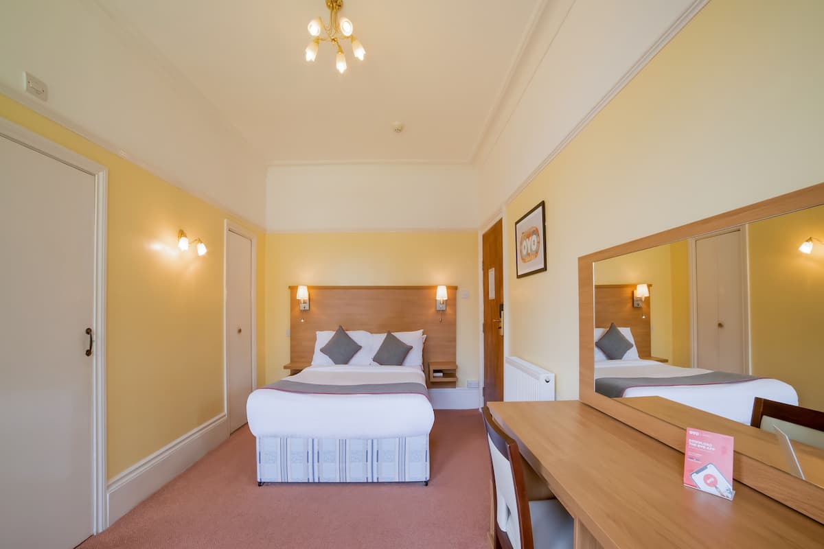 A hotel room with a bed, bedside tables, a desk, and a mirror.