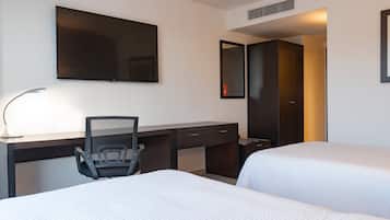 A hotel room with a desk, two beds, a chair, a TV, and a mirror.