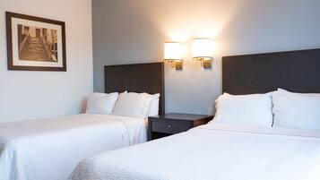 A hotel room with two beds, a nightstand, a framed picture on the wall, and wall-mounted lights.