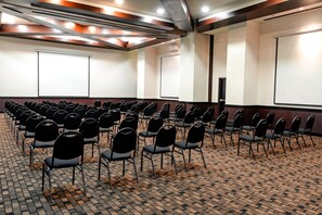 Un salón de conferencias con filas de sillas, una pantalla de proyector y suelo alfombrado.