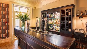 Uma área de bar com balcão de madeira, estante e diversos tipos de garrafas.