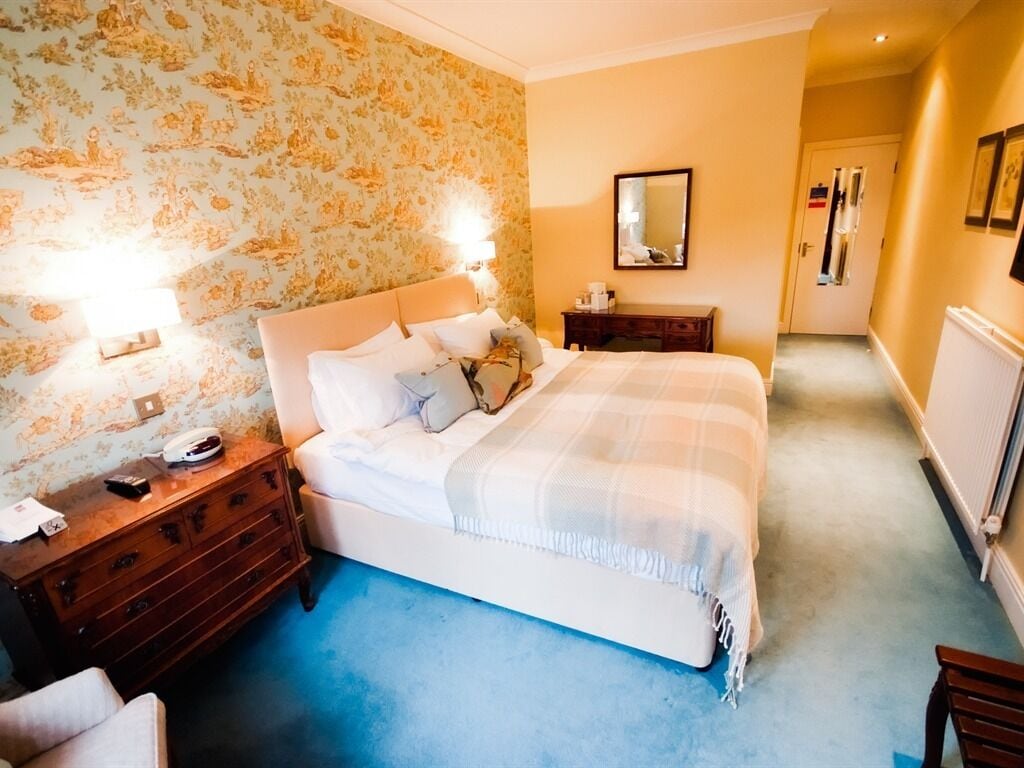 A bedroom with a large bed, a dresser, a nightstand, and a mirror on the wall.