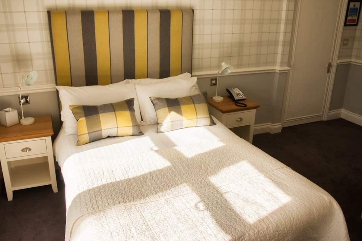 A neatly made bed with a striped headboard, a bedside table with a lamp, and a telephone.