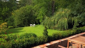 Um pátio com mesa e cadeiras de madeira, cercado por um muro de tijolos e vegetação exuberante.