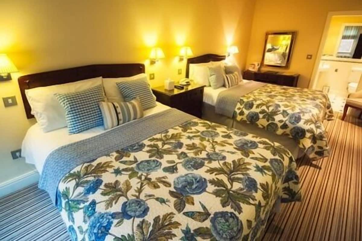 A hotel room with two beds, each with floral bedding, bedside lamps, and a mirror on the wall.