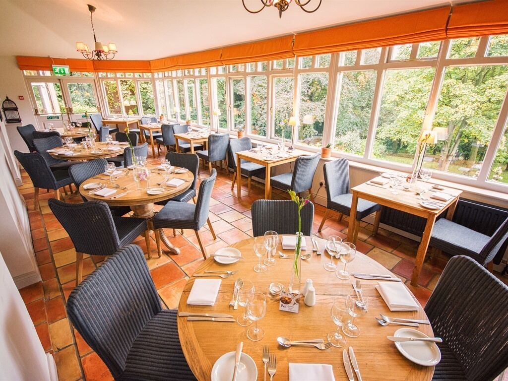 A restaurant with round tables and chairs, large windows, and a chandelier.