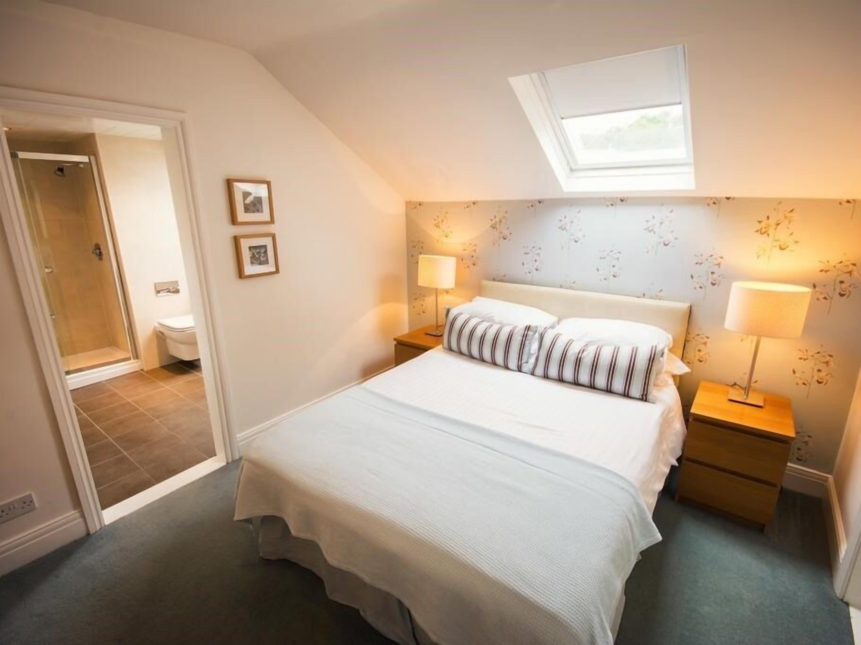 A bedroom with a large bed, two bedside tables, a skylight, and a shower area.