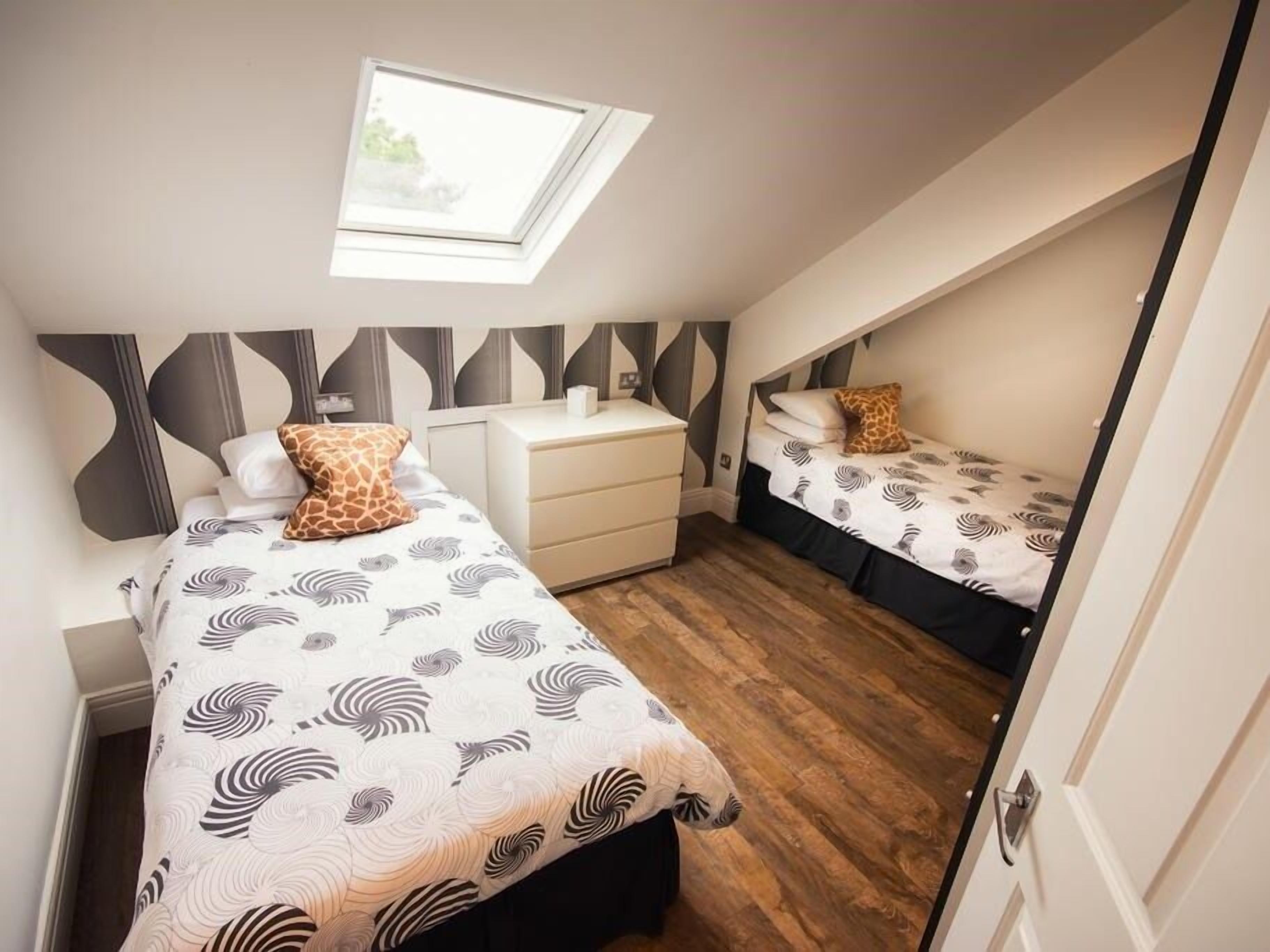 Une chambre à coucher de taille réduite, avec deux lits, un petit bureau et une lucarne.