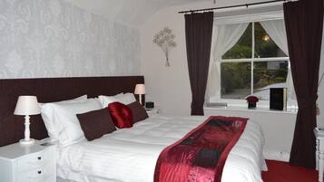 A neatly made bed with a white and red blanket, a bedside table with a lamp, and a window with curtains.