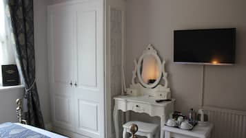 Un dormitorio con un armario grande, un tocador con espejo, una mesita de noche con bandeja y un televisor instalado en la pared.
