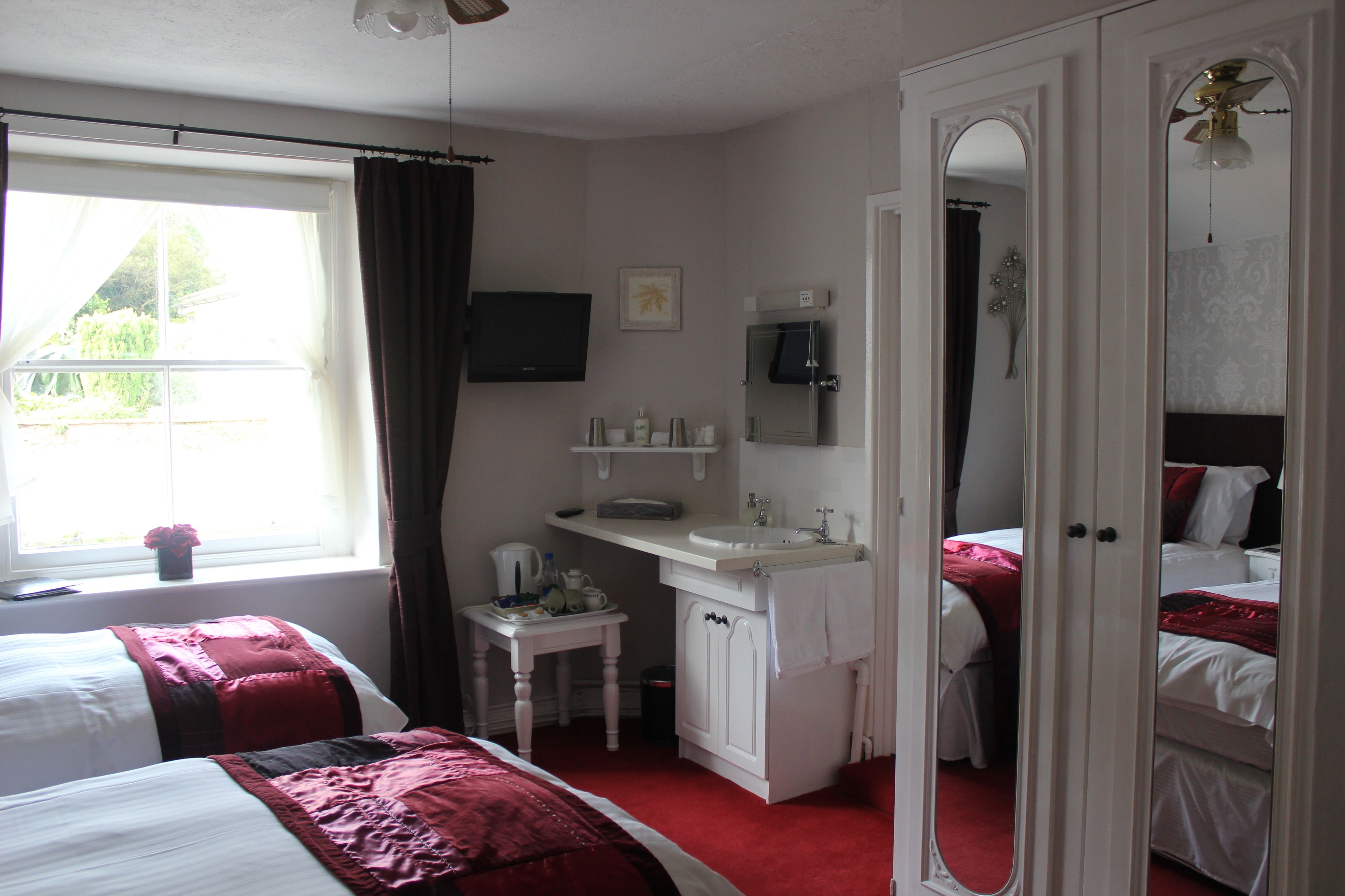A hotel room with two beds, a small bathroom, and a window with curtains.