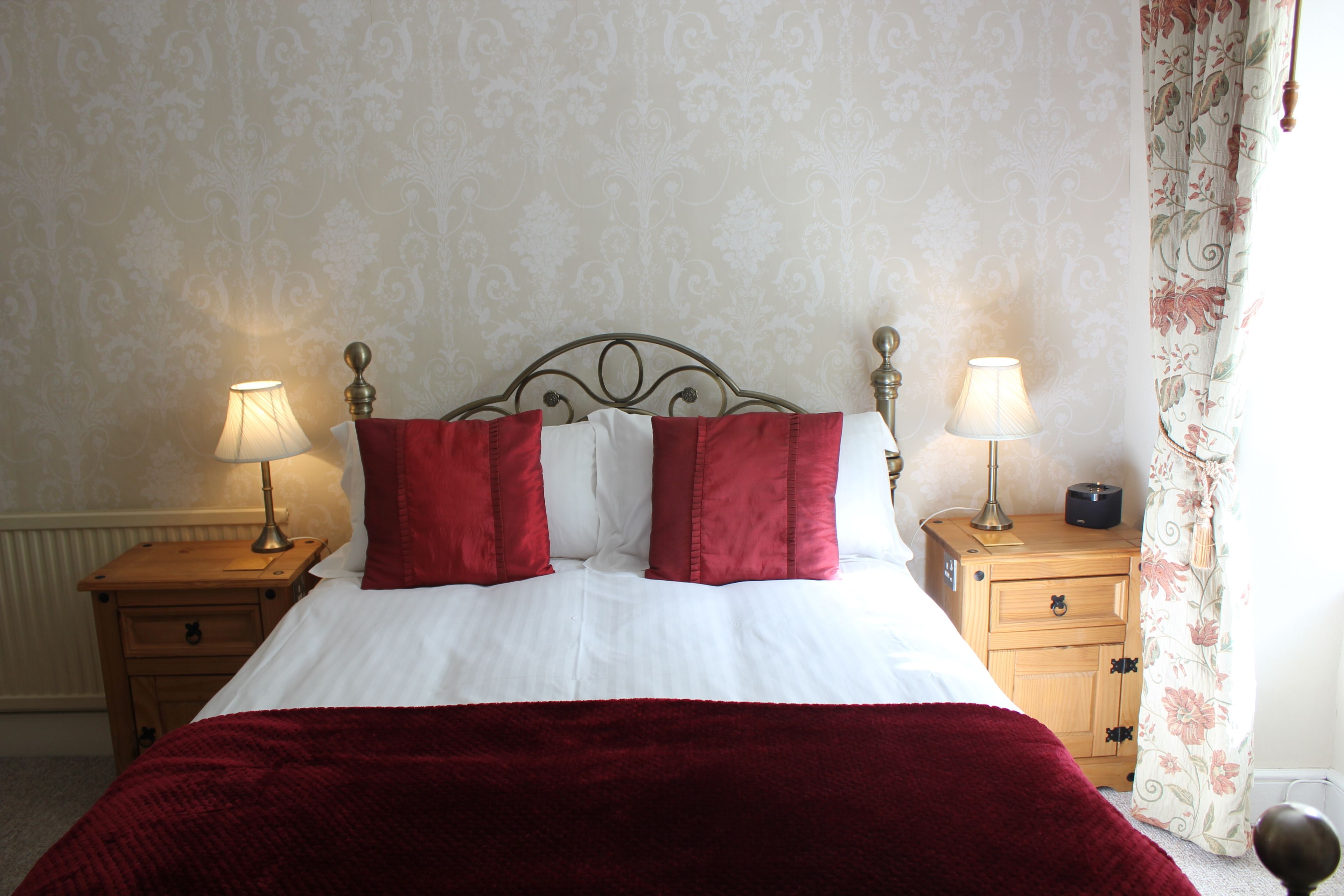 A neatly made bed with white and red bedding, two bedside lamps, and a wooden nightstand with a drawer.