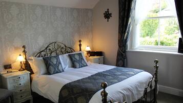 A neatly made bed with a patterned bedspread, two bedside tables with lamps, a nightstand, and a window with curtains.