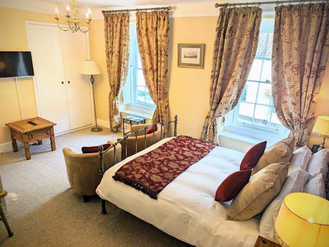 A bedroom with a bed, a chair, a table, a lamp, and curtains.