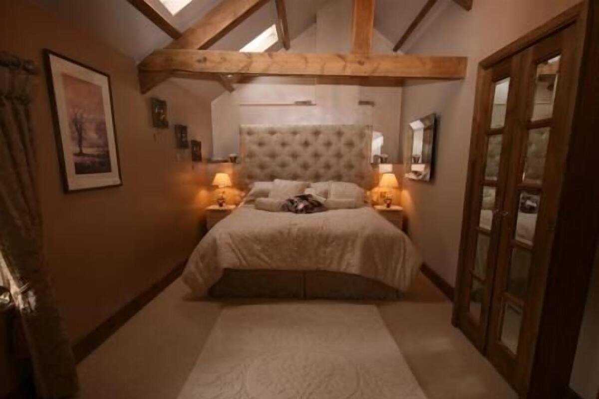 Ein Schlafzimmer mit einer gepolsterten Kopfteile, einem großen Bett, zwei Nachttischlampen, einem gerahmten Bild an der Wand und einer Holztür.