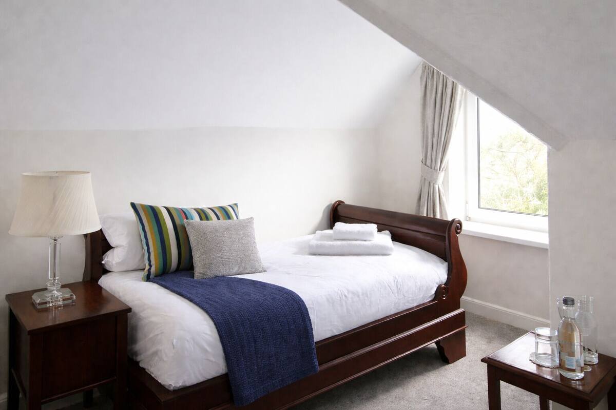 A neatly made bed with pillows, a bedside lamp, and a small table with a bottle and glass.