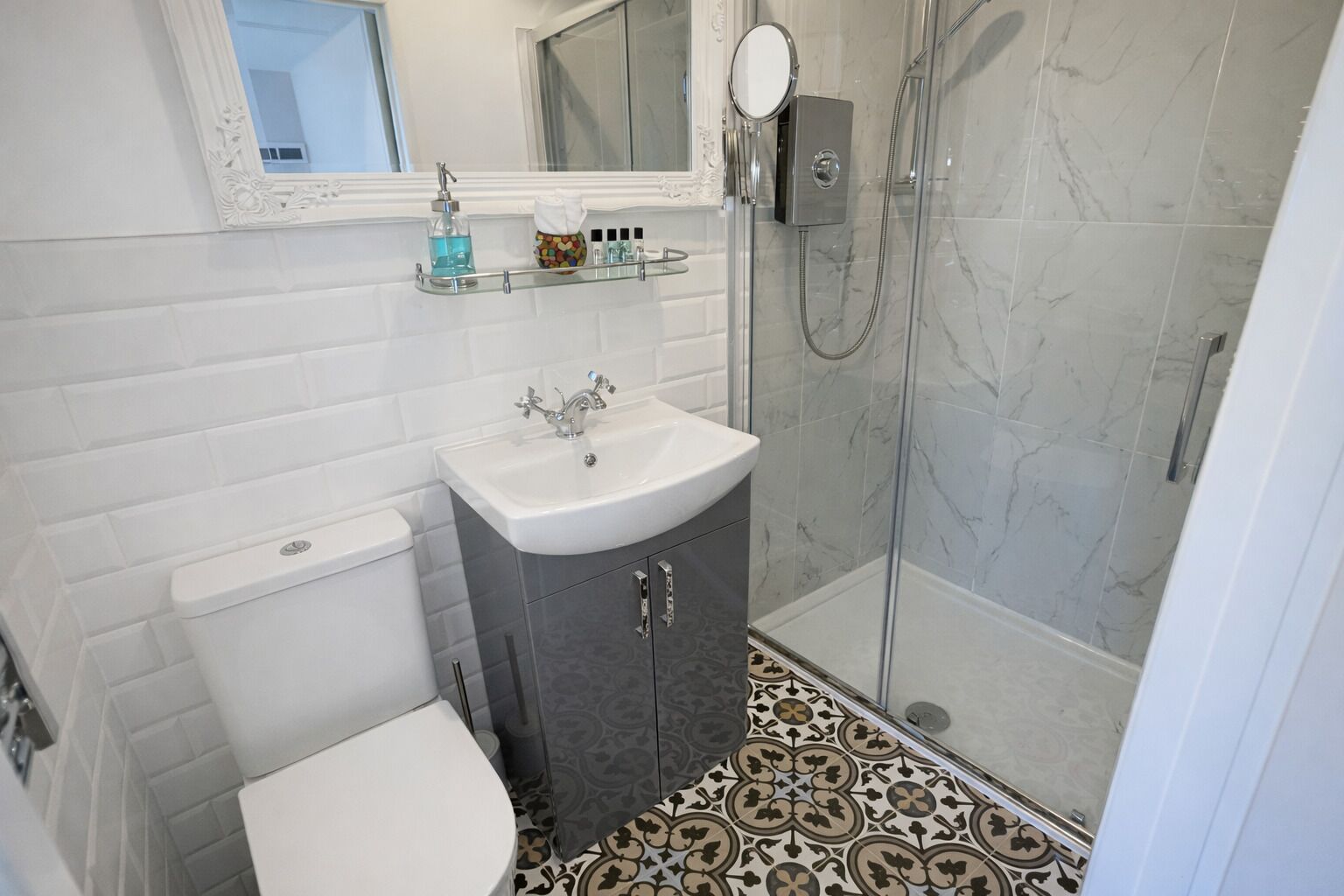 A bathroom with a toilet, sink, shower, and patterned floor tiles.