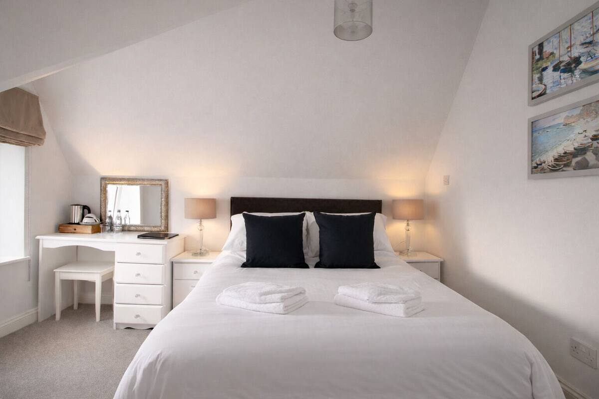 A bedroom with a bed, bedside tables, a desk, a mirror, and two paintings on the wall.